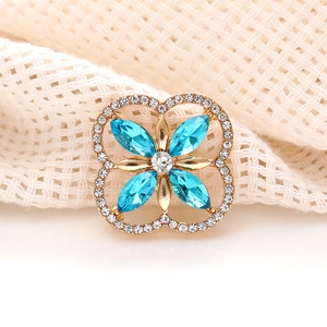 Macro detail of gold four-leaf clover brooch with blue marquise crystals and clear rhinestones