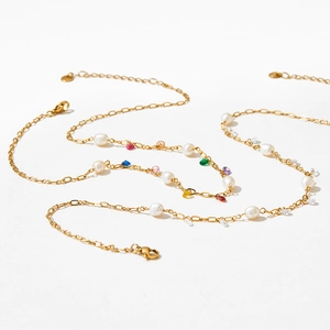 Detailed close-up of golden chain bracelet with multi-color gems and white pearls