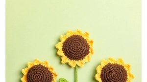 Detailopname van drie handgehaakte zonnebloemen met fijne garentextuur op een groene basis