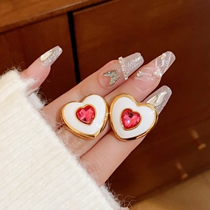 Close-up of heart-shaped gold earrings with white enamel and a central red zircon stone