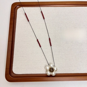 Macro view of French retro pearl flower pendant necklace with red beaded black cord