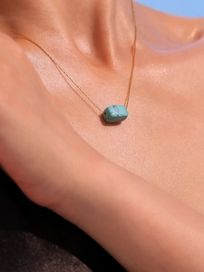 Close-up of a gold chain necklace with a natural turquoise pendant on a model's neck