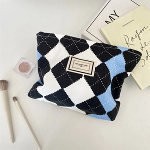 Macro shot of tricolor plaid velvet makeup bag with logo tag and cosmetic accessories
