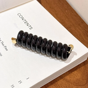 Détail d'un élastique spirale noir brillant avec attaches en métal doré sur un livre