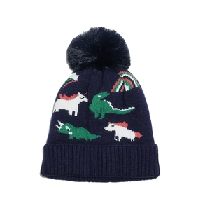 Close-up of navy knit hat with unicorn and dinosaur patterns and a plush faux fur pom