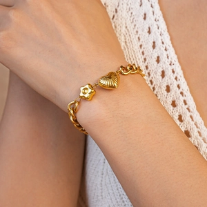 Detail of gold chunky chain bracelet with heart and flower charms on a wrist