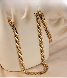 Detail of gold hip-hop chain set with square links displayed on silk fabric background