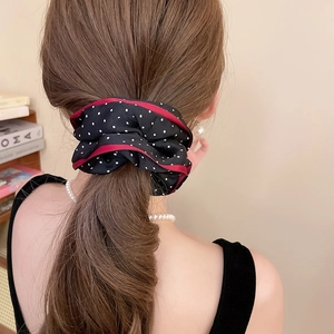 Rear view of a black polka dot fabric scrunchie with red edges on a low ponytail hair