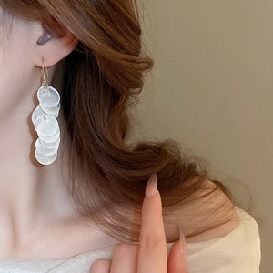Close-up of dangling white sequin tassel earrings worn for a summer beach look