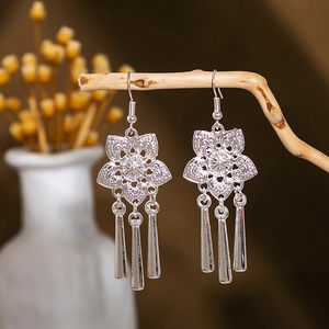 Detail of silver drop earrings with floral cutout and polished tassels on a wooden branch