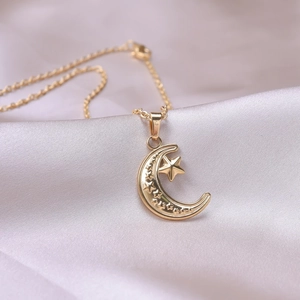 Macro shot of 18k gold plated moon and star necklace pendant on purple silk fabric