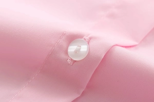 Détail macro du tissu en coton rose avec un bouton blanc à quatre trous et coutures