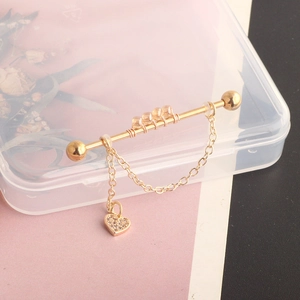 Detail of gold industrial barbell featuring a chain, heart pendant, and clear crystals