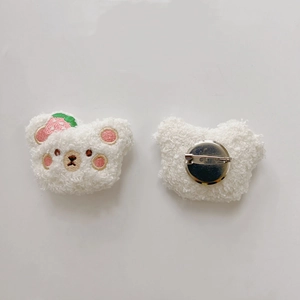 Detail of white plush bear brooch showing strawberry embroidery and metal pin clasp