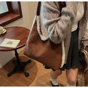 Brown faux suede tote bag with white plush trim worn by a model in a cozy cafe