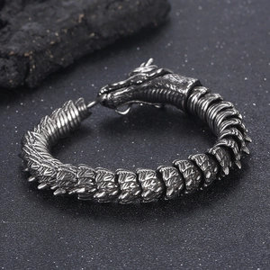 Detail of vintage silver dragon bracelet featuring scales and green eyes on black texture