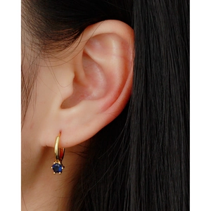 Close-up of gold hoop earring with a blue zircon drop pendant worn on ear