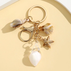 Close-up of golden keychain with luminous seashell and starfish pendants on beige background