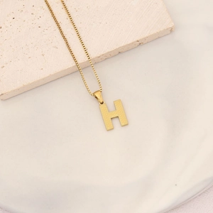 Detailed view of gold necklace featuring letter H pendant with dot texture on stone