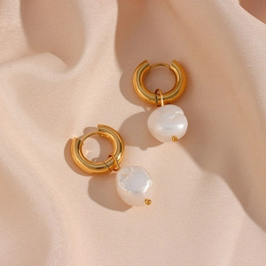 Gros plan de boucles d'oreilles dorées avec perles baroques sur tissu en soie champagne