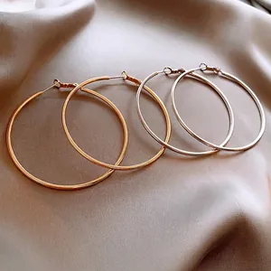 Minimalist gold and silver large hoop earrings displayed on elegant champagne silk fabric