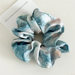 Macro detail of elastic satin hair scrunchie with blue marble tie-dye print pattern