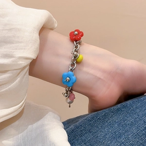 Close-up of stainless steel bracelet with colorful floral and pearl pendants on denim