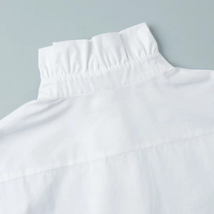 Close-up of elegant ruffled high neck and pleated collar detail on white cotton shirt