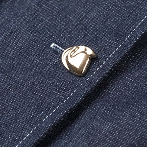 Gros plan sur un bouton doré irrégulier sur denim bleu foncé avec coutures blanches