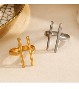 Nahaufnahme geometrischer H-förmiger Ringe in Gold und Silber auf strukturiertem Stoff