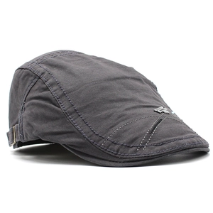 Detailed close-up of dark grey cotton beret showing metallic brand plate and stitching