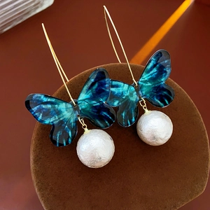 Makroaufnahme von blauen Schmetterlingsohrringen mit Perlen auf dunklem Samtständer