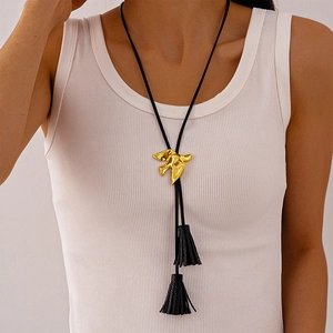 Detail view of a long necklace with a golden bird pendant and black tassel accents
