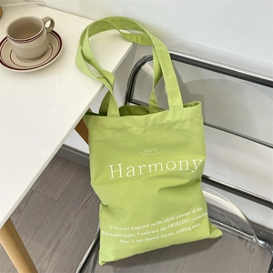 Detail of avocado green canvas tote bag with Harmony text print on a modern chair