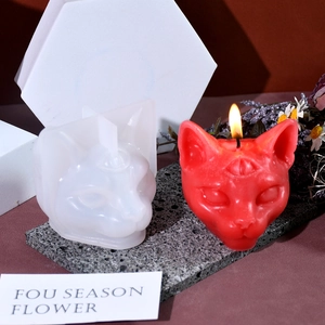 Detailed view of 3-eyed cat silicone mold and lit red scented candle on grey stone