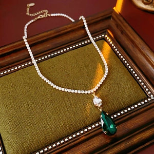 Detail of gold necklace featuring emerald green waterdrop pendant on vintage green lining