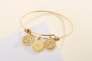 Detailed view of gold Cancer zodiac bangle with engraved Imaginative charm and symbols