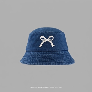 Detailed close-up of white embroidered bow on navy blue denim bucket hat texture