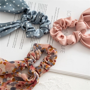Close-up of three long ribbon scrunchies in polka dot, floral, and pleated pink fabrics