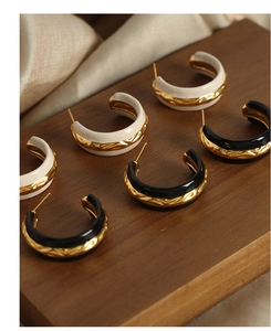 Detail of C-shaped hammered gold earrings with black and white enamel finishes