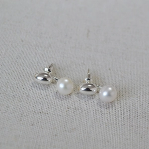 Detail shot of white freshwater pearl earrings with polished silver studs on fabric