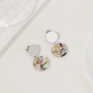 Detail of silver round earrings with natural rainbow abalone shell inlay on white surface