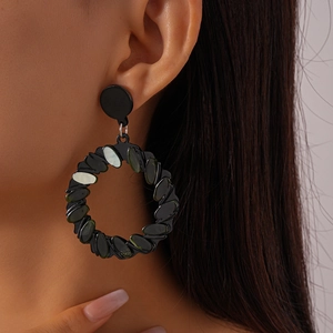 Detail of black acrylic geometric hoop earring with scale texture on female model