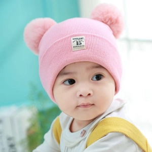 Detailed view of pink knitted baby hat featuring cute double fur pom-poms on the sides