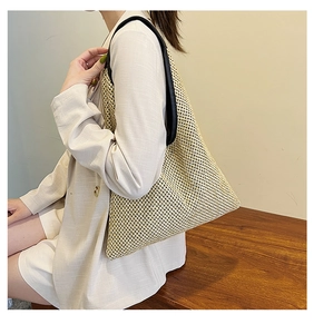 Detail of a large woven straw shoulder bag with black leather straps on a model