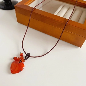 Close-up of a red agate heart pendant with a hand-woven brown cord on white background