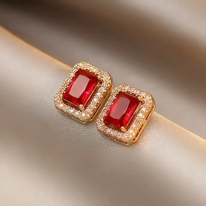 Macro shot of rectangular ruby earrings with zircon halo on champagne silk fabric