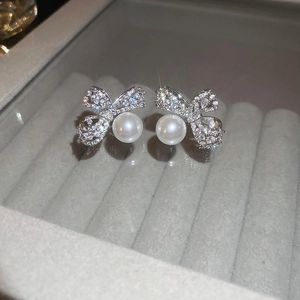 Macro shot of silver bow earrings with sparkling cubic zirconia and hanging white pearls