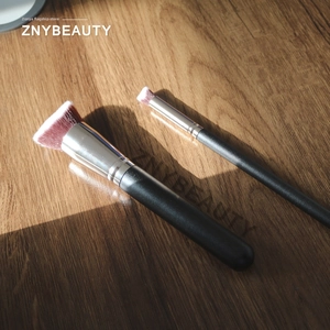 Macro shot of two gradient fiber makeup brushes with black handles on wooden background