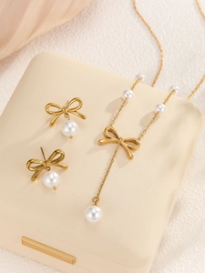 Close-up of golden bow pendant with elegant white pearl on a cream jewelry box